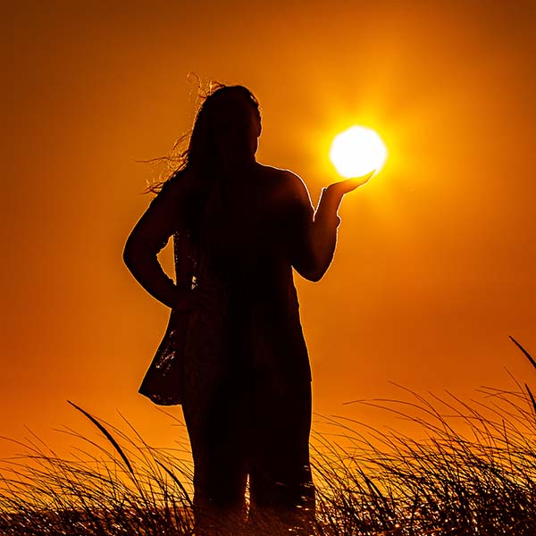 A girl with the sun above her hand during sunset