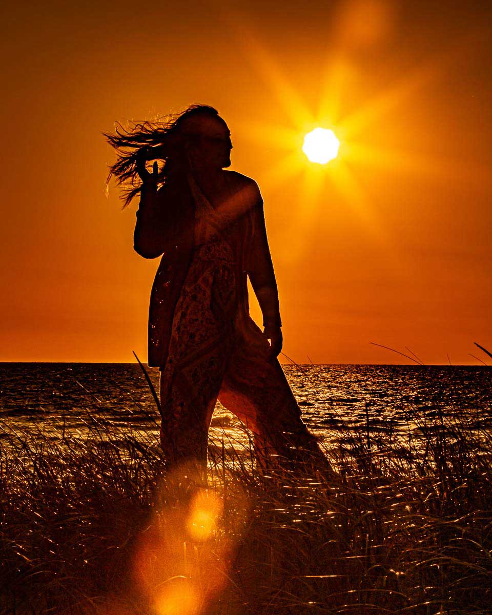 Girl standing in water with a sunset behind her